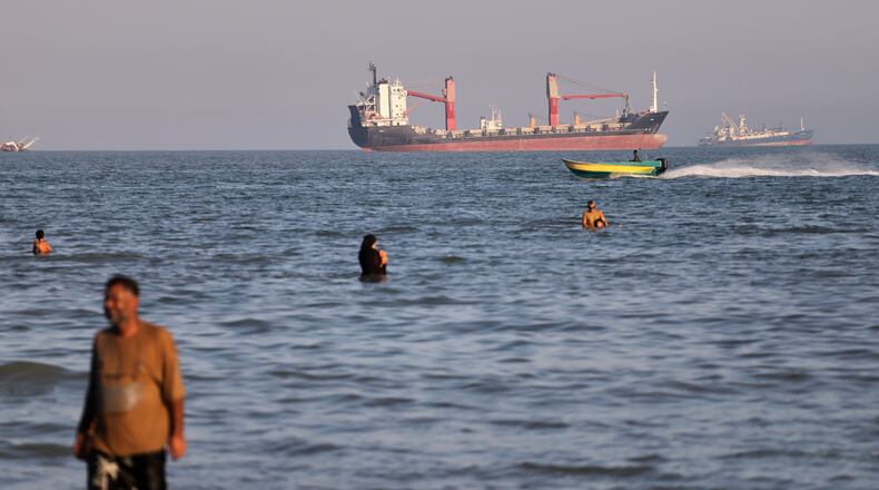Residents swim in the waters of the Strait of Hormuz as a small motorboat passes cargo ships and other commercial vessels offshore near Bandar Abbas, Iran, Wednesday, June 17, 2026. (Amirhosein Khorgooi/ISNA via AP)