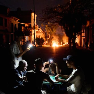 People illuminate themselves with their phones while playing dominoes as a fire set up by residents protesting against prolonged power outages burns on a street in Havana, Cuba, Thursday, May 14, 2026. (Ramon Espinosa/AP)