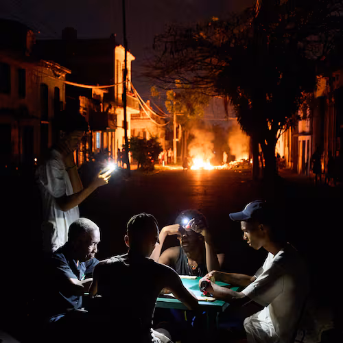 People illuminate themselves with their phones while playing dominoes as a fire set up by residents protesting against prolonged power outages burns on a street in Havana, Cuba, Thursday, May 14, 2026. (Ramon Espinosa/AP)