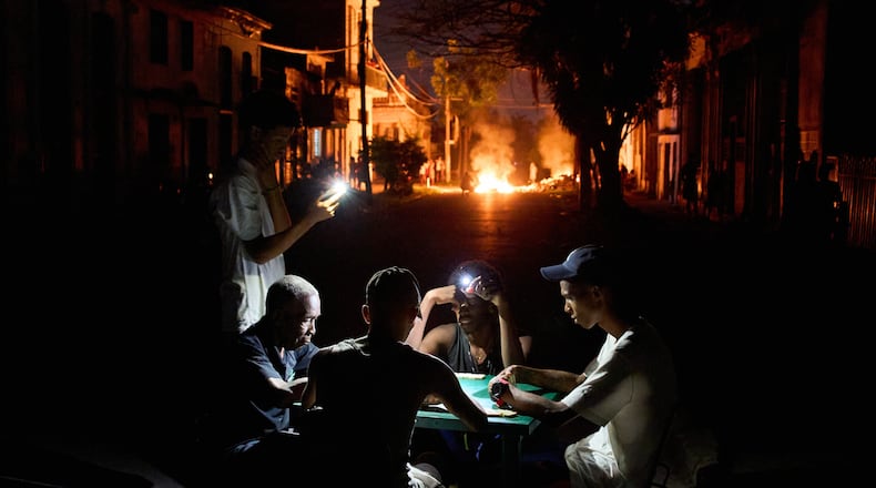 People illuminate themselves with their phones while playing dominoes as a fire set up by residents protesting against prolonged power outages burns on a street in Havana, Cuba, Thursday, May 14, 2026. (Ramon Espinosa/AP)