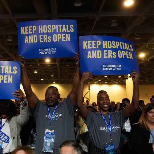 FILE - People supporting Billionaire Tax Now hold up signs at the 2026 California Democratic Party State Convention in San Francisco, Feb. 21, 2026. (AP Photo/Jeff Chiu, File)