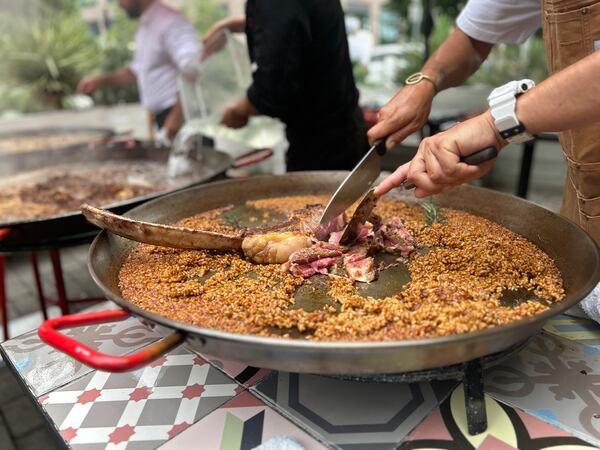 Tomahawk steak being sliced on top of a paella pan filled with rice.