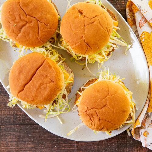 A platter of four turkey smash burgers, topped with shredded lettuce and American cheese, is shown with a floral cloth napkin beside it.