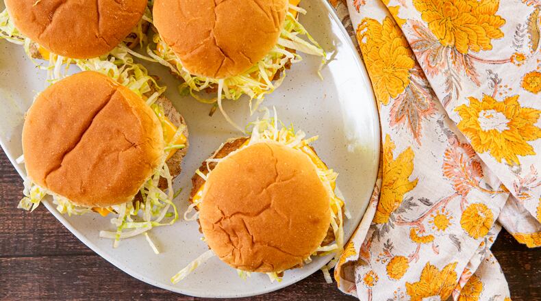 A platter of four turkey smash burgers, topped with shredded lettuce and American cheese, is shown with a floral cloth napkin beside it.