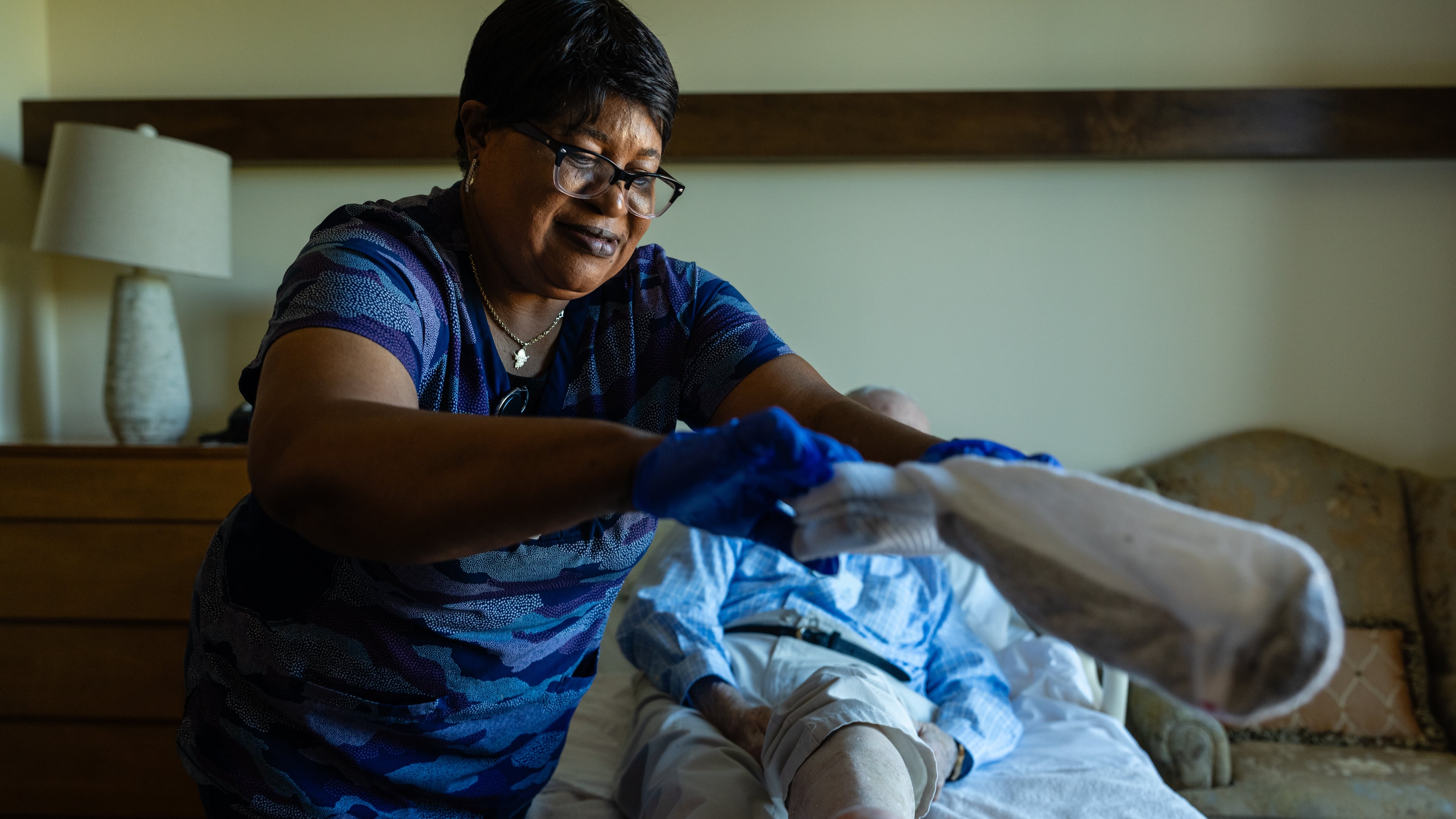 Jackie Conteh, an advanced care partner originally from Sierra Leone, helps Donald Goodness, 92, put on fresh socks in his apartment at Goodwin House Alexandria, Thursday, Oct. 16, 2025, in Alexandria, Va. (AP Photo/Eric Lee)