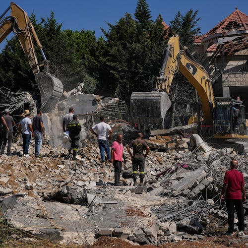 People watch rescue workers use excavators as they search for victims under the rubble of a building destroyed in an Israeli airstrike in the southern village of Kfar Rumman, Lebanon, Monday, Sept. 7, 2026. (AP Photo/Mohammed Zaatari)