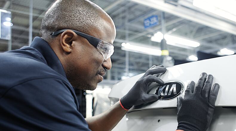Kia worker attaches the brand name to a brand new Kia.