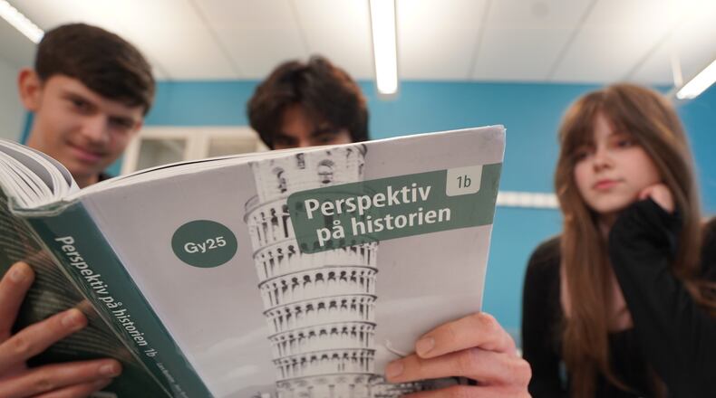 High school students from left, Vasilije Stjepanovic, Aslan Ozhan Kilicasan and Melina Sallahi pose with a history text book at Malmo Borgarskola high school in Malmo, Sweden, May 21, 2026. (AP Photo/James Brooks)
