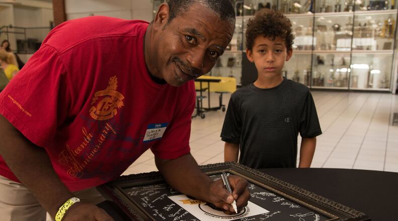 Central Gwinnett High graduate Wayne Maxey, accompanied by his son, signs a memory book during the recent celebration to mark the school’s 60th anniversary. CONTRIBUTED