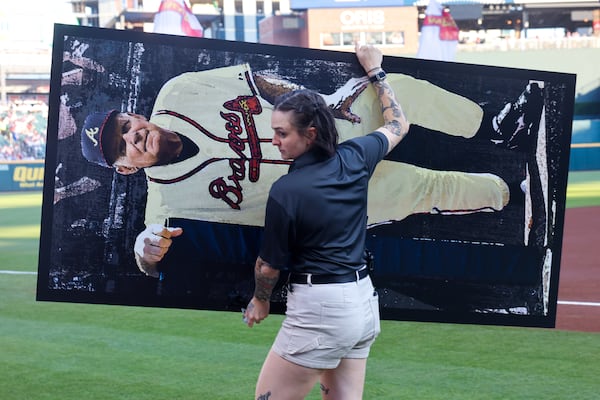 A removes a poster of Bobby Cox after a pregame ceremony at Truist Park. (Arvin Temkar/AJC)