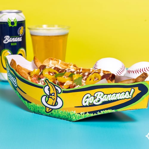 A loaded hot dog in a Savannah Bananas vessel is flanked by a couple of baseballs and a beer.