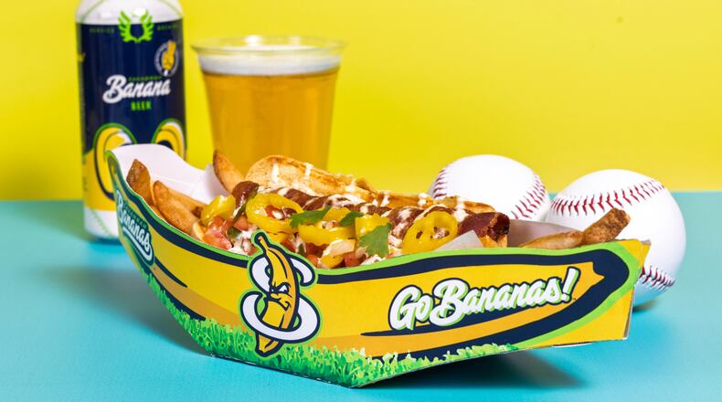 A loaded hot dog in a Savannah Bananas vessel is flanked by a couple of baseballs and a beer.