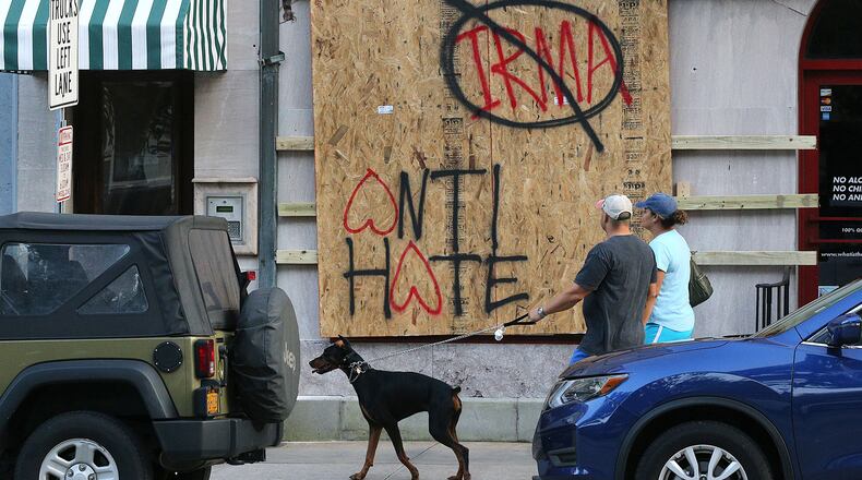 Eric and Nicole Zajkowski, who just evacuated from their home in Coral Springs, Fla., walk their dog Neeko past a boarded-up store on Savannah's Bay Street Friday. Curtis Compton/ccompton@ajc.com