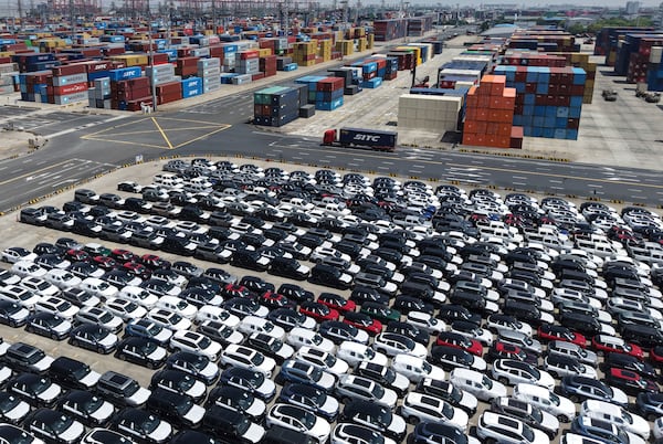 A truck moves past new vehicles for export at a port in Shanghai, China on Sunday, April 27, 2025. (Chinatopix Via AP)