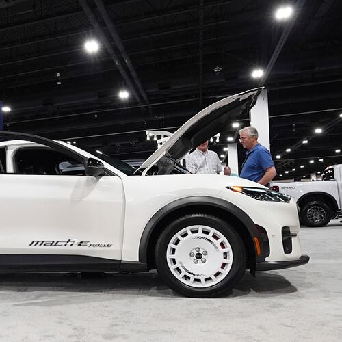 FILE - Shoppers look over a 2025 Mach-E electric utility vehicle in the Ford display at the Colorado Auto Show, April 17, 2025, in Denver. (AP Photo/David Zalubowski, File)