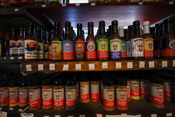 A close-up shot of two rows of products on the wall of the hot sauce shop. The rows are absolutely packed with bottles. The top row contains bottles of hot sauces that have brightly colored labels. The second row contains shakers of seasonings.