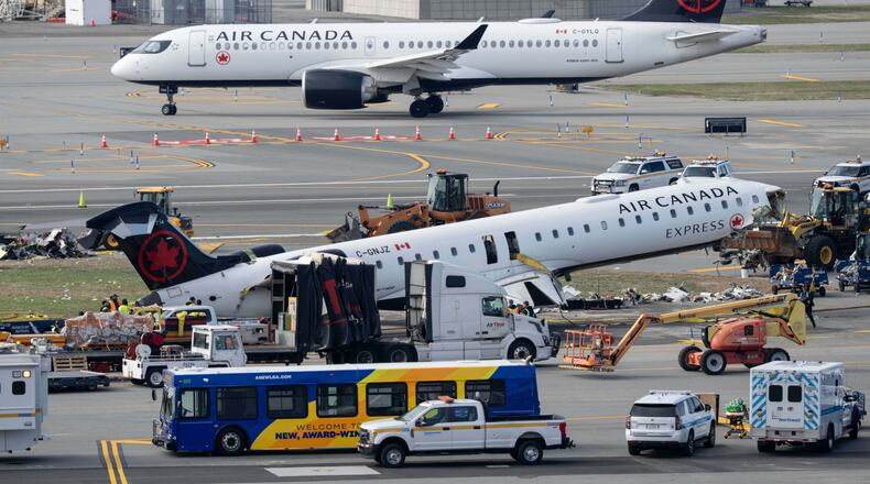 An Air Canada Express jet taxis past the wreckage of an Air Canada Express jet, Wednesday, March 25, 2026, as maintenance crews prepare to move the plane from the runway where it had collided with a Port Authority fire truck Sunday night at LaGuardia Airport, in New York. (AP Photo/Yuki Iwamura)