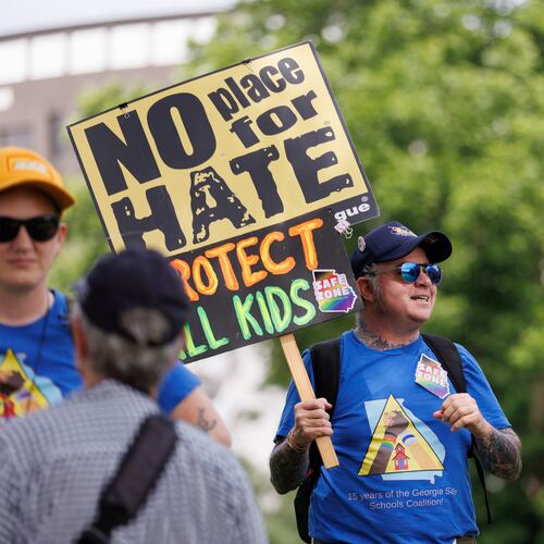 A small group of protestors rally before a school board meeting in Decatur on Thursday. SJ, his activist name, wears stickers and a T-shirt showing him as a “safe zone.” Protesters are upset with what they believe is a lack of transparency around building an early learning center and the district's connection to the superintendent's controversial podcaster husband. (Estela Muñoz/AJC)