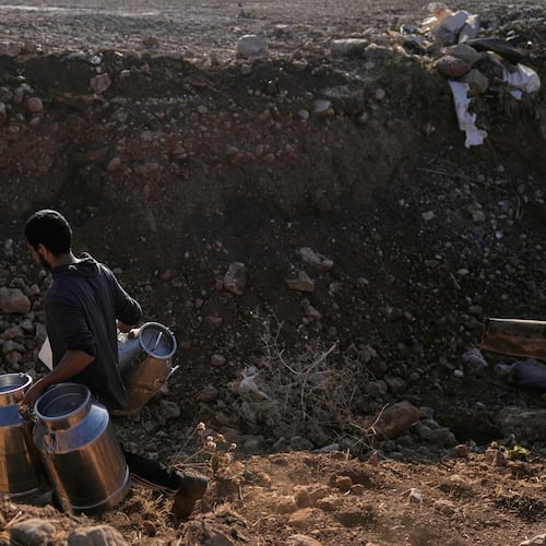 A Palestinian farmer carries containers of milk from their livestock across a trench dug by the Israeli army in a road leading to the West Bank hamlet of Khirbet Ras al-Ahmar, southeast of Tubas, on their way to sell it Saturday, Sept. 19, 2026. (AP Photo/Majdi Mohammed)