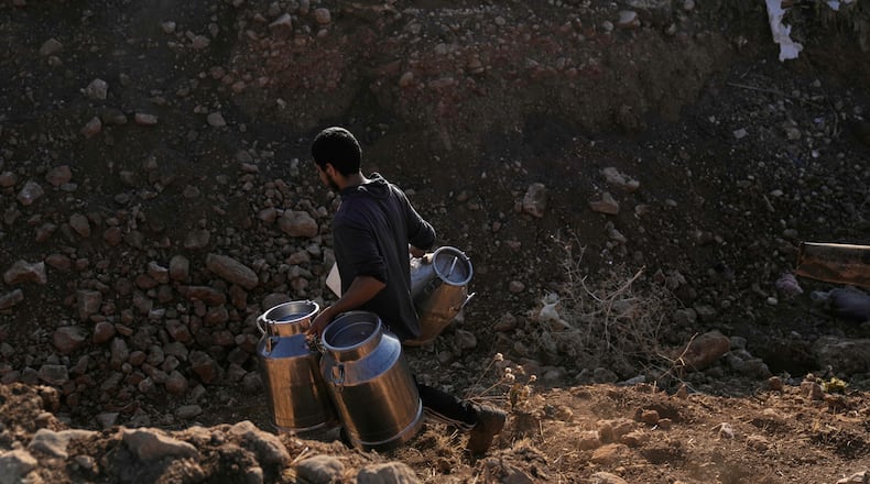 A Palestinian farmer carries containers of milk from their livestock across a trench dug by the Israeli army in a road leading to the West Bank hamlet of Khirbet Ras al-Ahmar, southeast of Tubas, on their way to sell it Saturday, Sept. 19, 2026. (AP Photo/Majdi Mohammed)