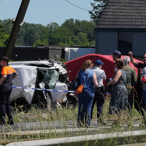 Police and residents gather around a level crossing where a train collided with a van in Buggenhout, Belgium, Tuesday, May 26, 2026. (AP Photo/Marius Burgelman)