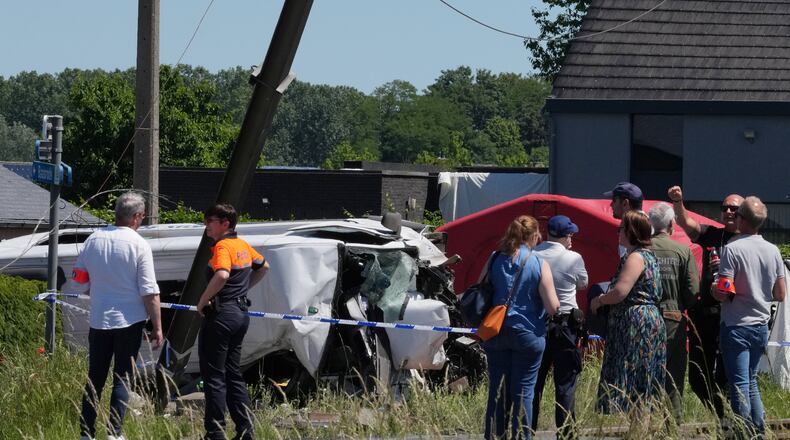 Police and residents gather around a level crossing where a train collided with a van in Buggenhout, Belgium, Tuesday, May 26, 2026. (AP Photo/Marius Burgelman)