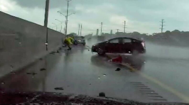 A state trooper sprints to avoid a hydroplaning car Monday in South Florida.