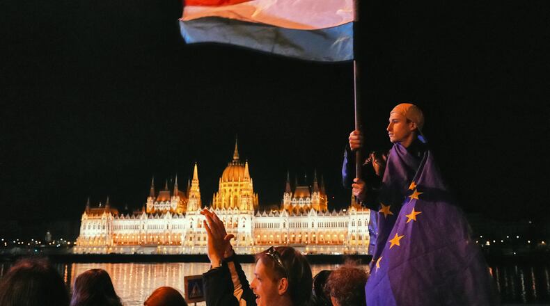 A man wrapped in the European Union flag waves a Hungarian flag, backdropped by the parliament building, early Monday April 13, 2026 as people celebrate Peter Magyar ousting Prime Minister Viktor Orban after 16 years in power. (AP Photo/Sam McNeil)