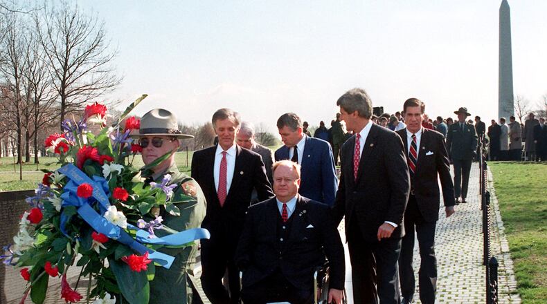 In this file photo, then-U.S. Sen. Max Cleland, D-Ga. (in wheelchair), and fellow senators — (left to right) Bob Kerrey, D-Neb.; John McCain, R-Ariz.; Charles Hagel, R-Neb.; John Kerry, D-Mass.; and Chuck Robb, D-Va. — walk along the Vietnam Veterans Memorial wall behind the wreath they would lay to commemorate the 15th anniversary of groundbreaking for the memorial. All six senators served in Vietnam, and Cleland lost both legs and an arm in that war. He was awarded the Silver Star, the Bronze Star, and the Soldier’s Medal. He appears briefly in the introduction of the documentary series. (Photo by Rick McKay/Washington Bureau)