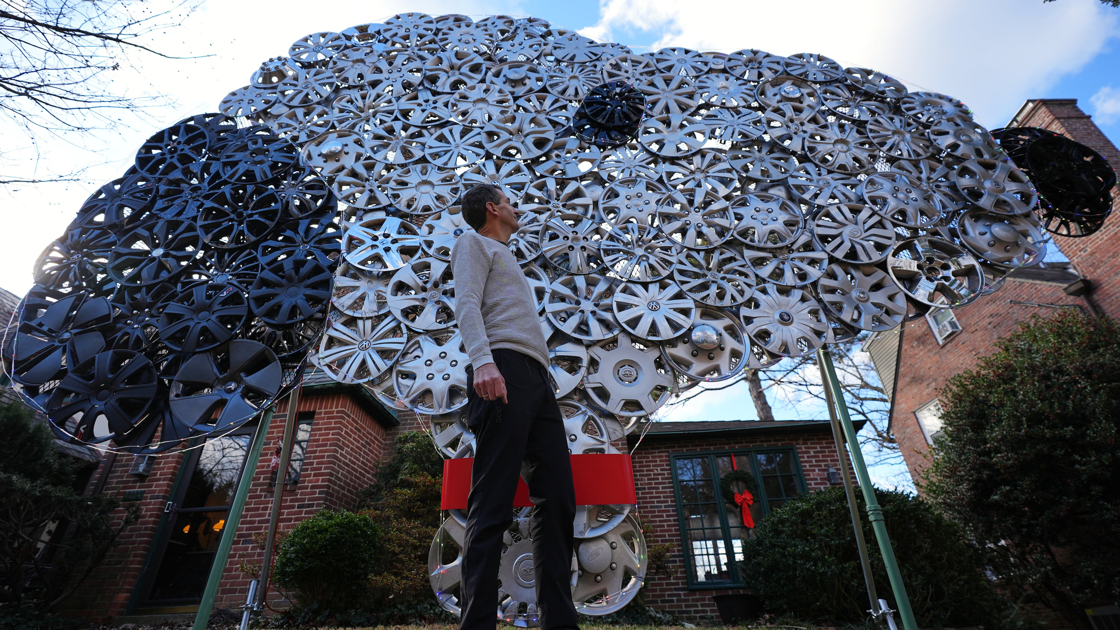 Cyclist Barnaby Wickham poses for a portrait in front of his art structure made from hubcaps, Thursday, Dec. 11, 2025, at his home in Baltimore. (AP Photo/Stephanie Scarbrough)