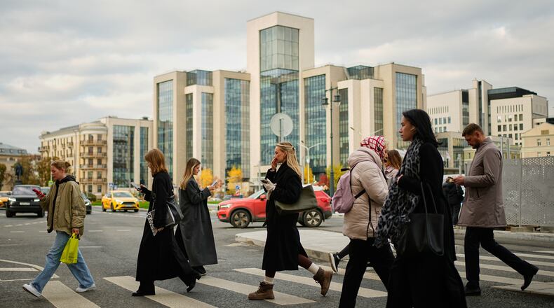 People cross a street, with Russian oil company Lukoil's headquarters seen in the background, in Moscow, Russia, Thursday, Oct. 23, 2025. (AP Photo/Pavel Bednyakov)