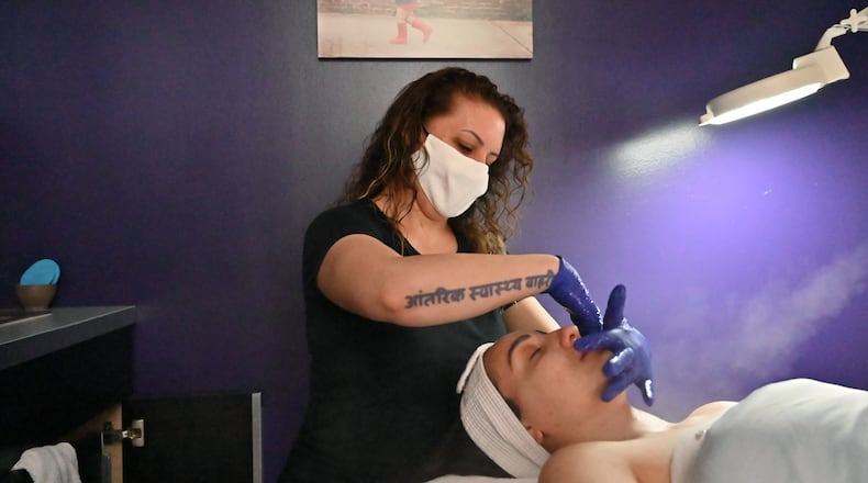 Paris Campeau gives a facial massage at Indigo Wellness Spa in Kirkwood on Wednesday to Virginia Carter, who asked that she wear latex gloves. Campeau, who owns the spa, didn’t open her boutique when the governor said she could a month ago, but now, with bills piling up and some clients ready to come by, she’s giving it a shot. (Hyosub Shin / Hyosub.Shin@ajc.com)