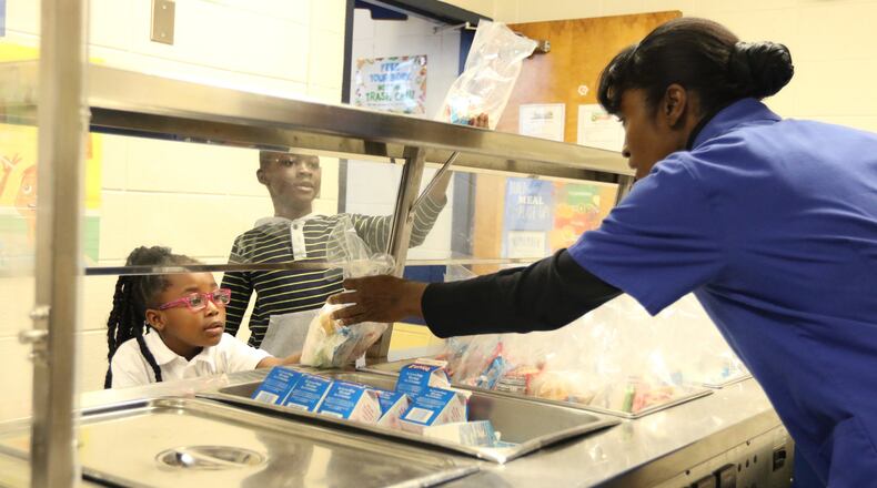 Kindergartener Azaria Youg, left, and second grade student James Nyamekye grab their after-school meals in the cafeteria at Burnett Elementary School in Douglasville on Feb. 15. Douglas County Schools has begun providing early dinners to students who stay after school for activities. EMILY HANEY / emily.haney@ajc.com