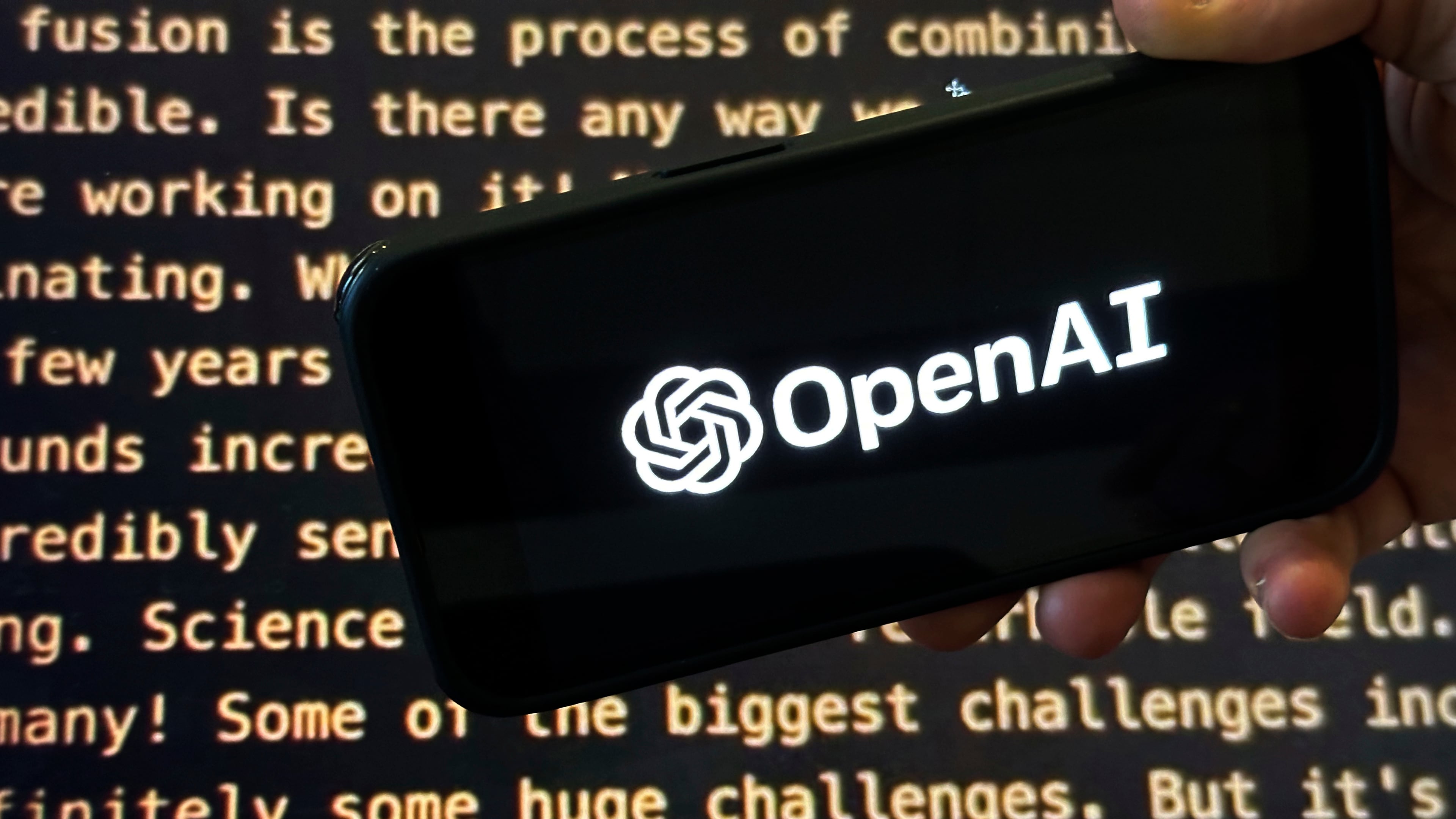 FILE - The OpenAI logo appears on a mobile phone in front of a screen showing part of the company website in this photo taken on Nov. 21, 2023 in New York. (AP Photo/Peter Morgan, File)