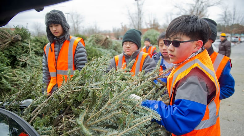 James Suh (right) helps his fellow Boy Scouts from Troop 2000 unload a Christmas tree from a car as they volunteer during Bring One for the Chipper at the Home Depot off of States Bridge Rd. in Johns Creek on Saturday, January 4, 2014.