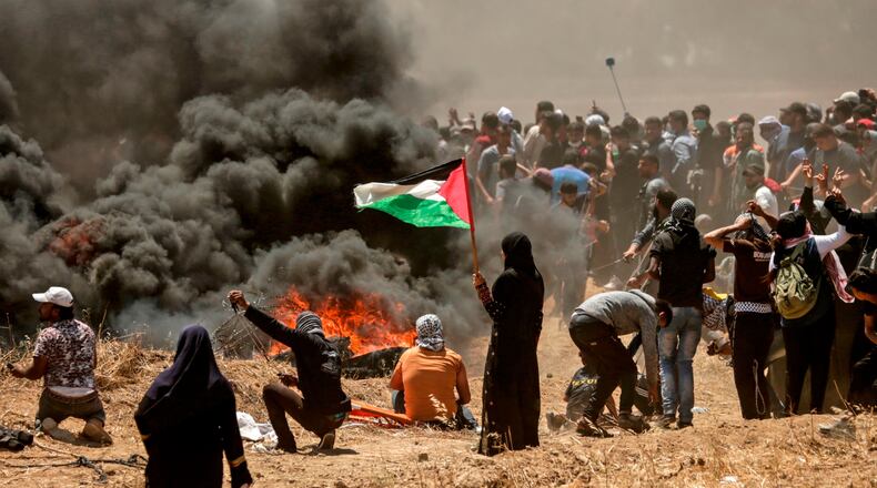 A Palestinian woman holding her national flag looks at clashes with Israeli forces near the border between the Gaza strip and Israel east of Gaza City on May 14, 2018, as Palestinians protest over the inauguration of the U.S. embassy following its controversial move to Jerusalem.