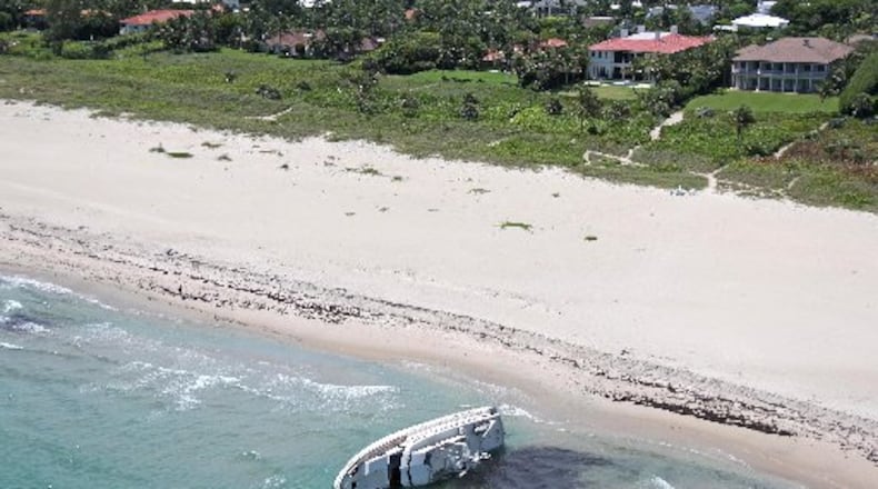 Time Out, a 72-foot yacht, lies on its port side on the beach at the northern tip of Palm Beach, where homes and mansions rise beyond the dune. Photo by Brian Lee, courtesy WoollyMammothPhoto.com.