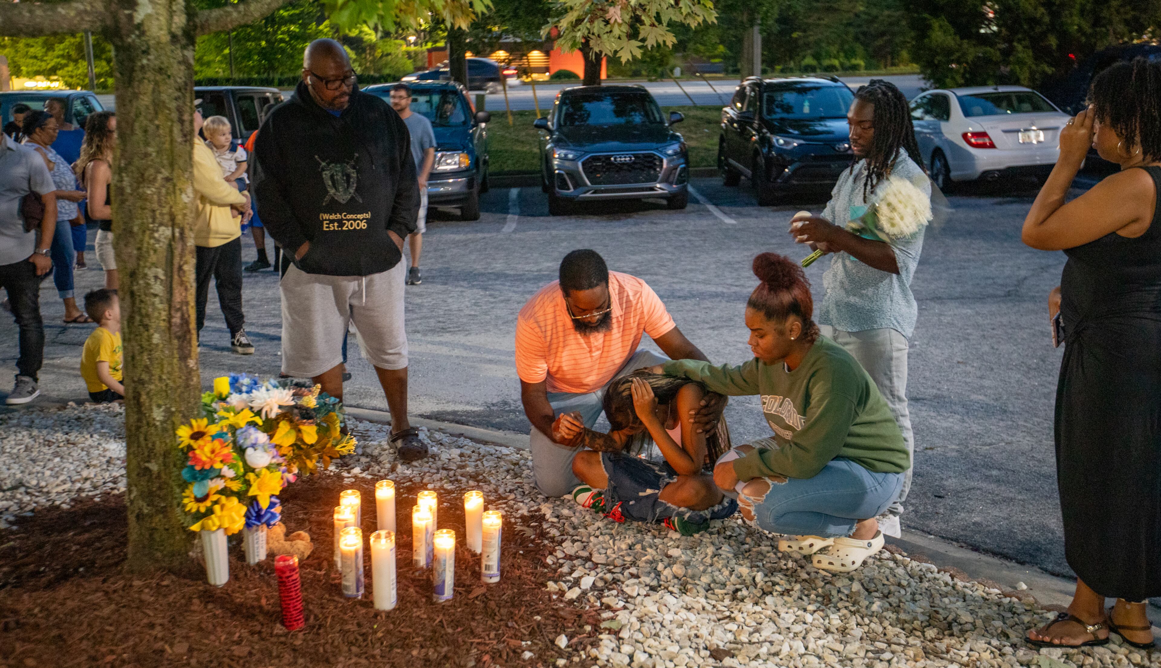 Jerry Johnson is seen holding Mecca Johnson (seated center) as they mourn the loss of 16-year-old Jacob Johnson at a candlelight vigil and balloon release in 2023. (Jenni Girtman for the AJC)