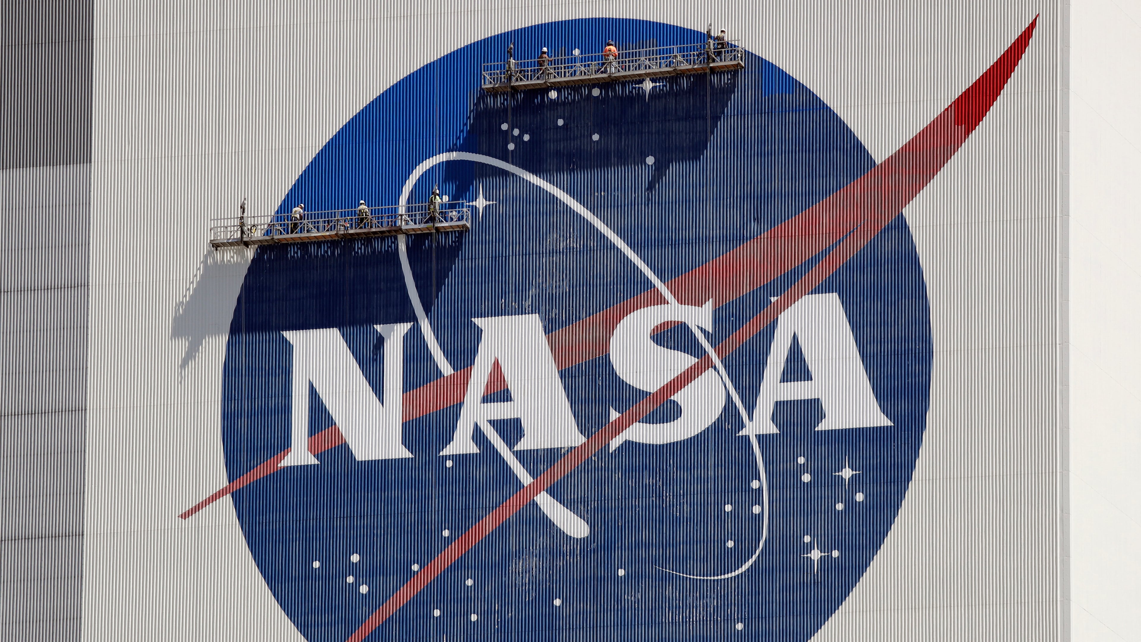 FILE - Workers on scaffolding repaint the NASA logo near the top of the Vehicle Assembly Building at the Kennedy Space Center in Cape Canaveral, Fla., May 20, 2020. (AP Photo/John Raoux, File)