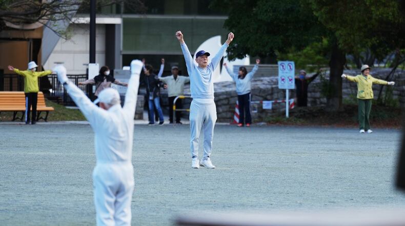 People perform a stretching exercise while listening to music and guidance from radio at a public park in Tokyo, Monday, April 6, 2026. (AP Photo/Hiro Komae)