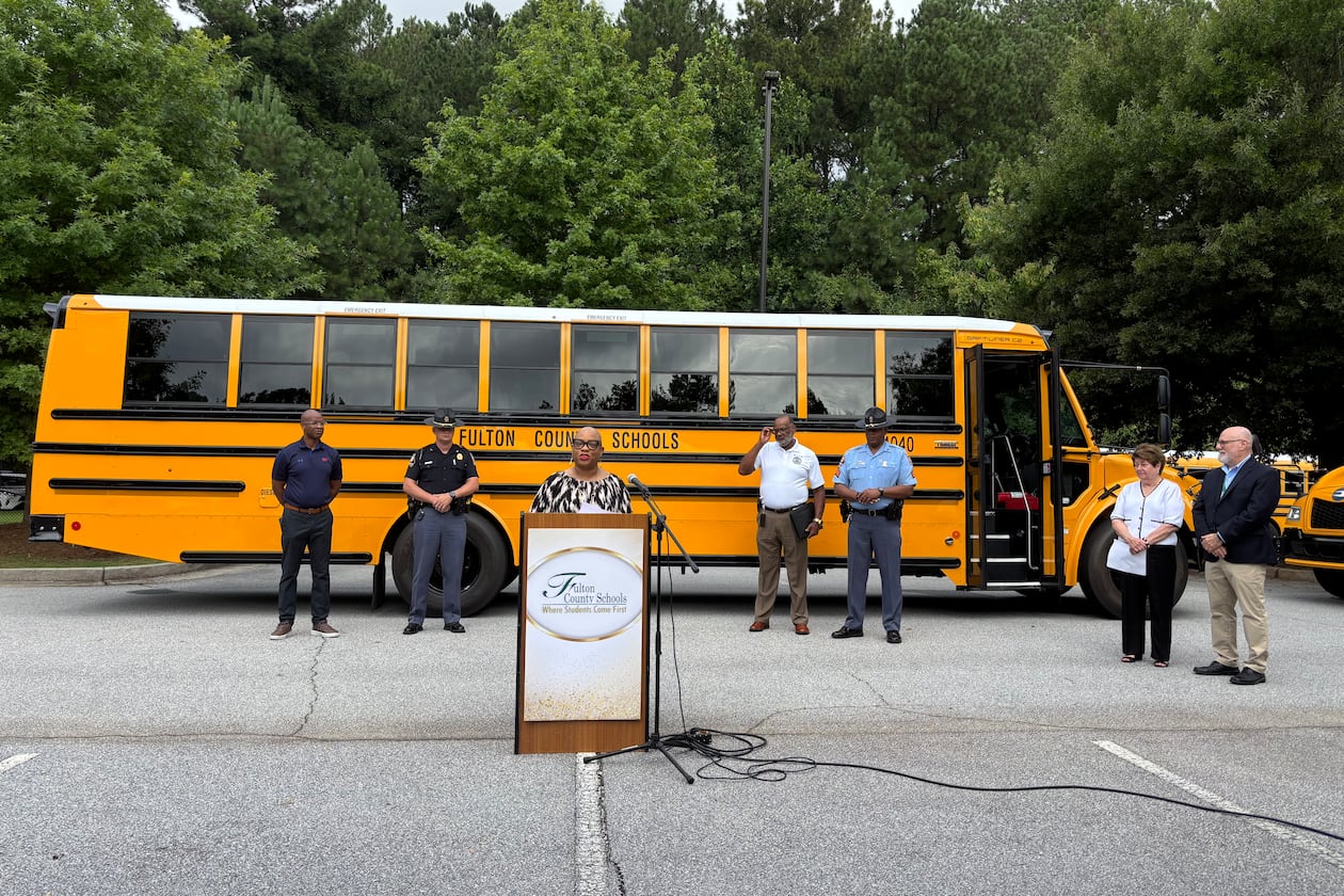 Various officials speak at a press conference in front of two Fulton County school buses.