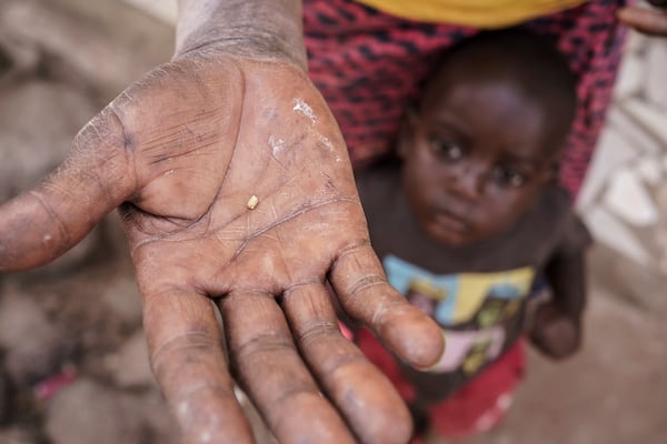 Sadio Camara's son clings to her as she holds a crumb of gold she extracted using mercury at her home in the Kedougou region of Senegal on Thursday, Jan. 16, 2025. (AP Photo/Annika Hammerschlag)