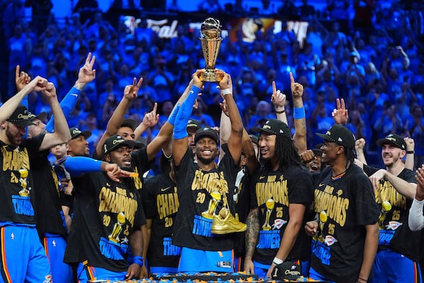 Oklahoma City Thunder guard Shai Gilgeous-Alexander (center) holds up the Finals MVP trophy while celebrating a title with his team.