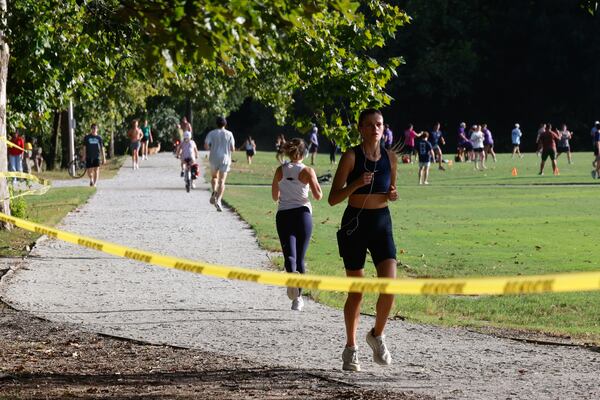 A runner jogs past crime scene tape in Piedmont Park in Atlanta on Sept. 9, 2026. Police have detained two men and are searching for a third person after a dispute escalated to gunshots. (Arvin Temkar/AJC)