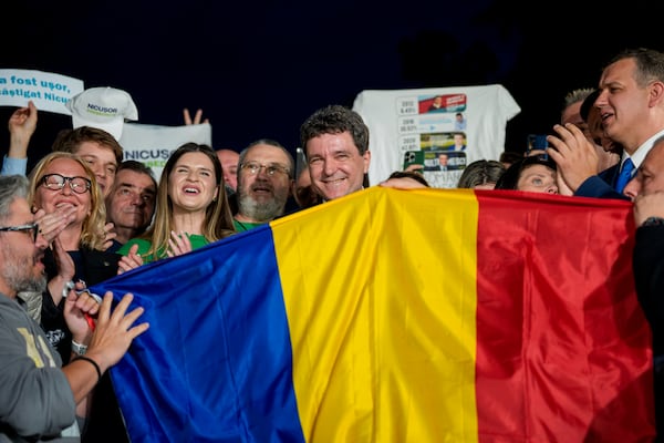 Presidential candidate Nicusor Dan, center, poses behind a Romanian flag after polls closed for the second round of the country's presidential election redo in Bucharest, Romania, Sunday, May 18, 2025. (AP Photo/Andreea Alexandru)