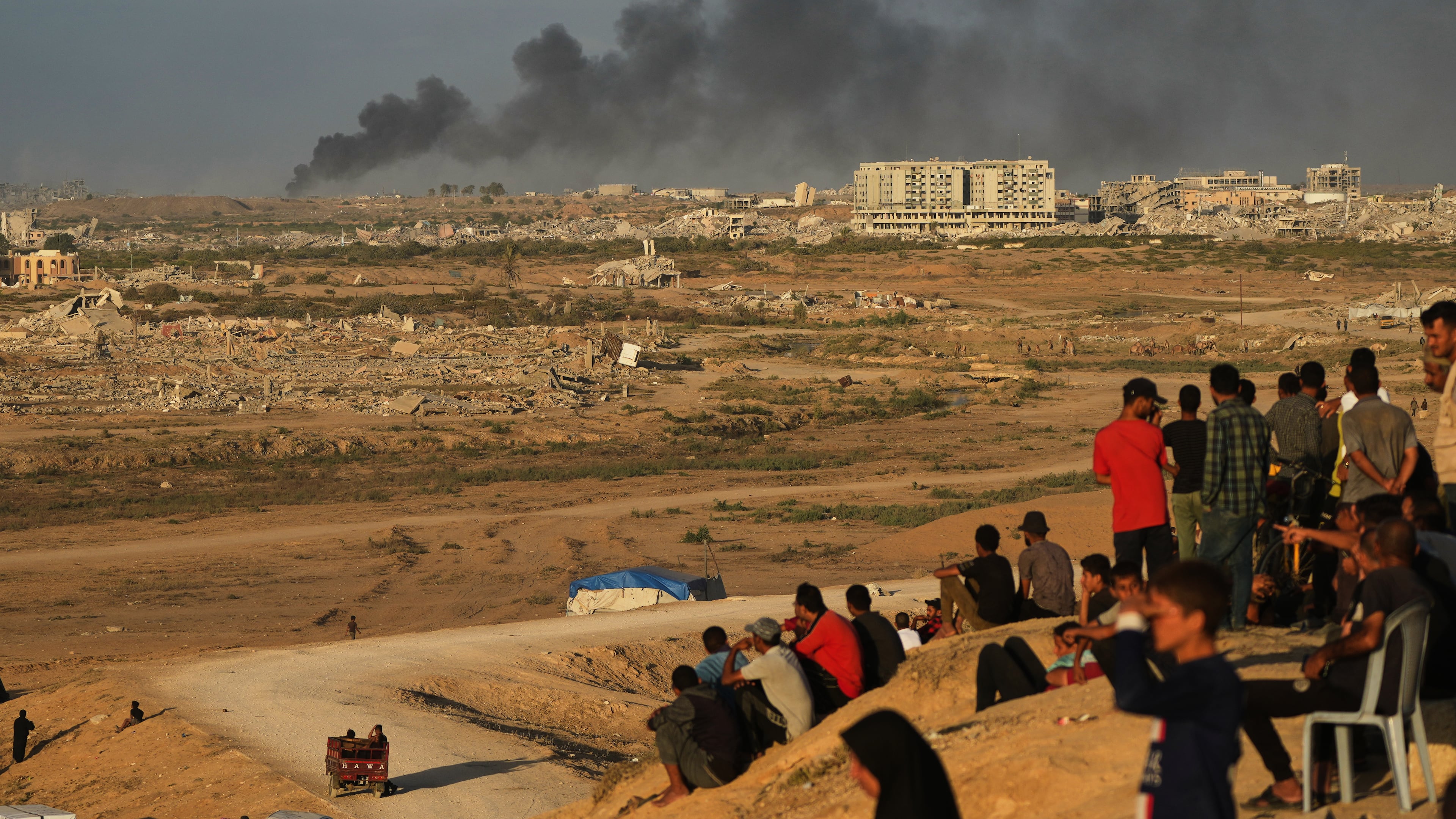 Displaced Palestinians watch smoke rise after Israeli military strikes as they gather on the coastal road near Wadi Gaza, in the central Gaza Strip, Thursday, Oct. 9, 2025. (AP Photo/Abdel Kareem Hana)