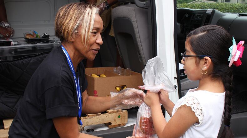 Rita Williams, the founder and CEO of One 2 One Educational Support, left, gives Isis Romero food as part of the Book Mobile initiative by Gwinnett County Public Schools, Atlanta Community Food Bank and One 2 One to bring books and food to children, at the Centre at Peachtree Corners apartments on Friday, July 20. Jenna Eason / Jenna.Eason@coxinc.com