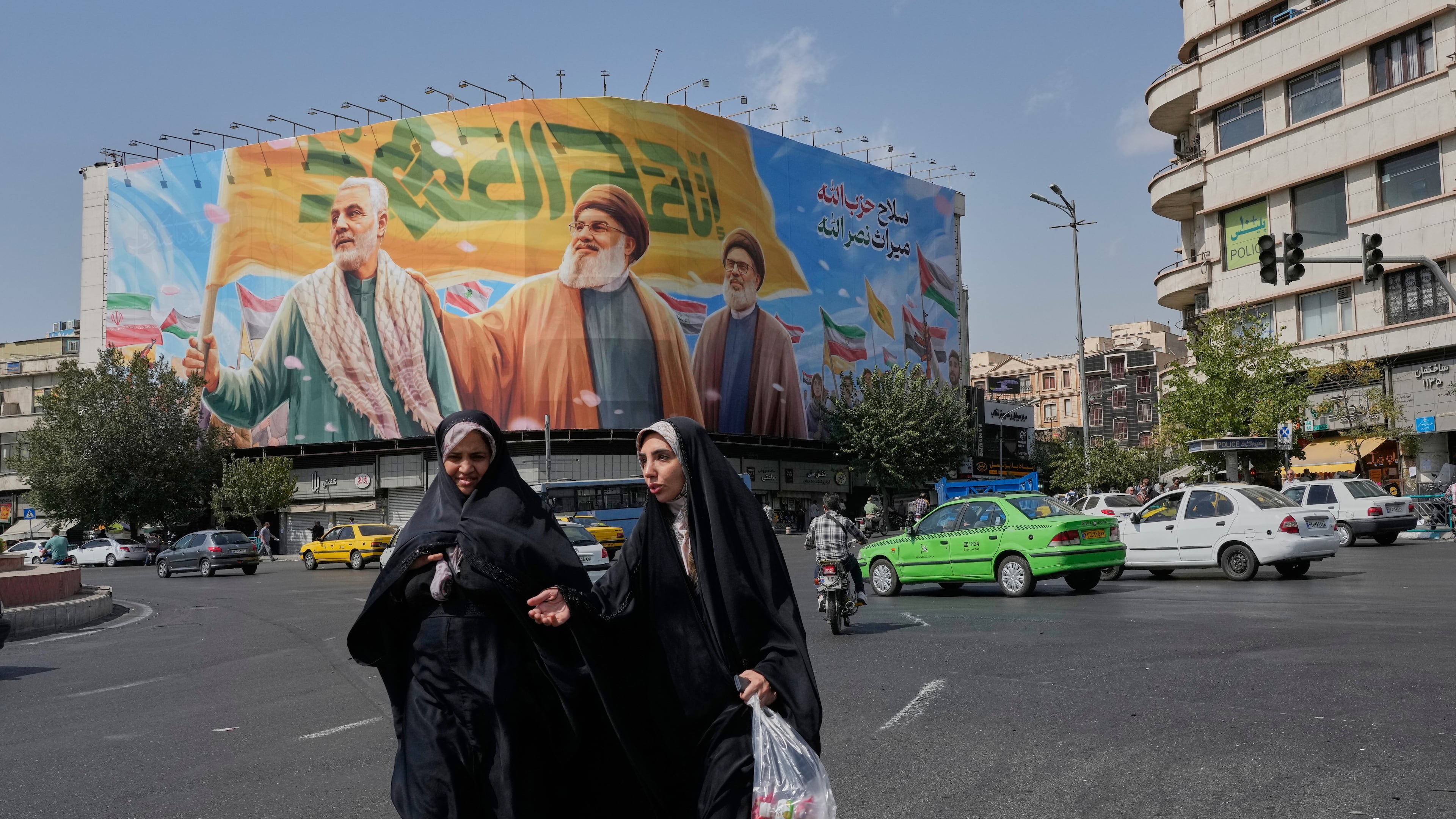 Two women walk past a huge banner showing the late commander of the Iran's Revolutionary Guard expeditionary Quds Force, Gen. Qassem Soleimani, who was killed in a U.S. drone attack in 2020, and two late Hezbollah leaders Hassan Nasrallah, center, and Hashem Safieddine, who were killed in Israeli airstrikes in 2024, at the Enqelab-e-Eslami (Islamic Revolution) square, in Tehran, Iran, Saturday, Sept. 27, 2025. (AP Photo/Vahid Salemi)