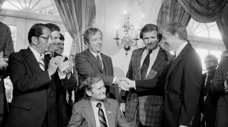 FILE - President Jimmy Carter, right, shakes hands with the Michigan delegation, in Washington, April 24, 1980, who were present for the signing by Carter of a bill that would enable Volkswagen to operate an auto assembly plant in a Detroit suburb. Sen. Don Riegle, D-Mich., next to Carter, and Michigan Senate Majority Leader William Faust seated center, look on. (AP Photo, File)