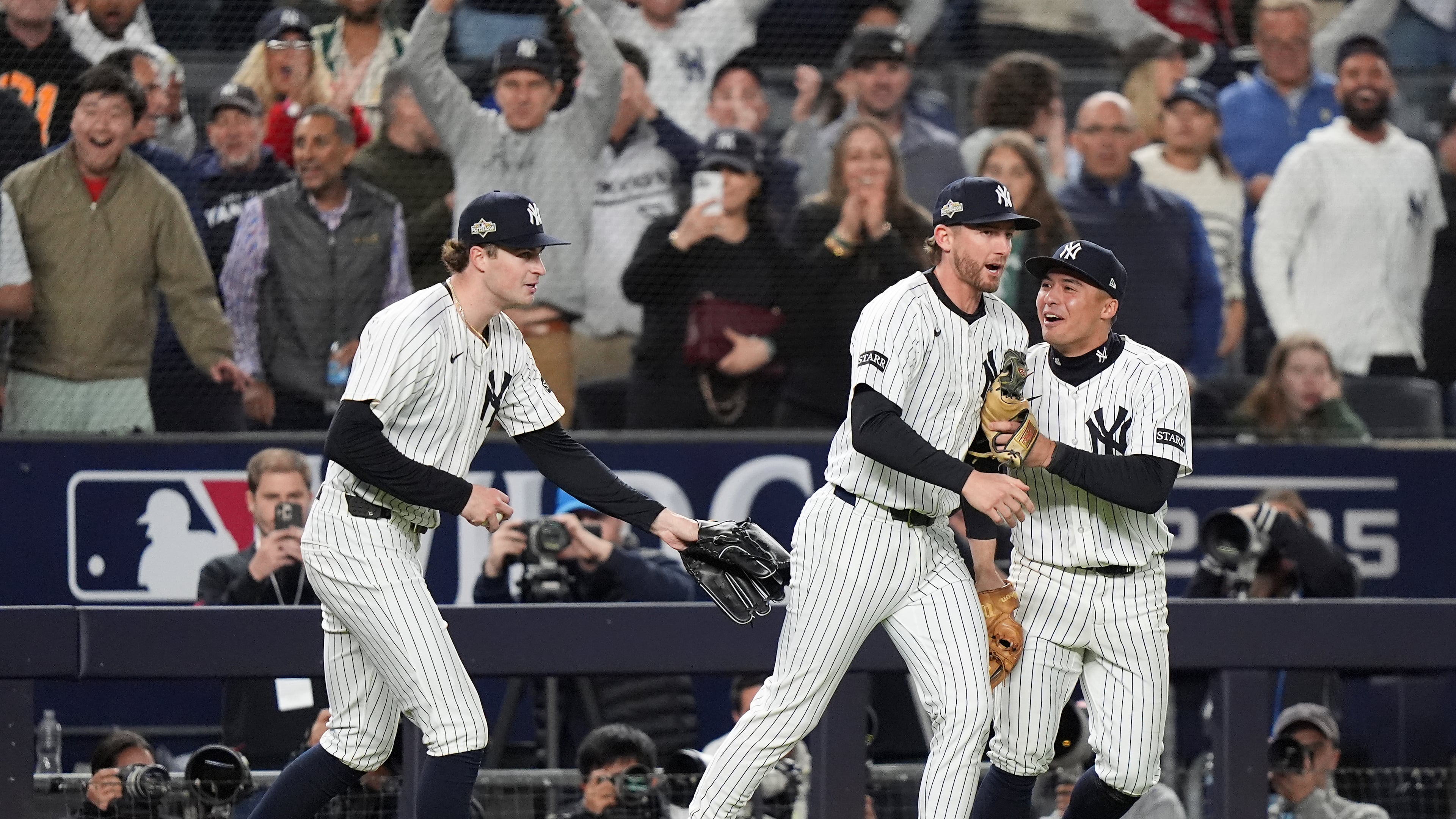 New York Yankees third base Ryan McMahon, center, is congratulated by pitcher Cam Schlittler, left, and shortstop Anthony Volpe after making a catch over the Boston Red Sox dugout during the eighth inning of Game 3 of an American League wild-card baseball playoff series, Thursday, Oct. 2, 2025, in New York. (AP Photo/Frank Franklin II)